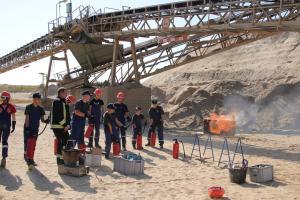 Mitglieder der Jugendfeuerwehr üben auf einem Betriebsgelände den sicheren Umgang mit Feuerlöschern an einem gasbetriebenen Feuerlöschtrainer.
