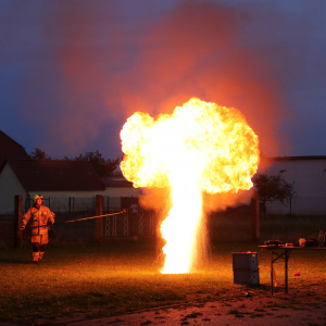 Brandschutz Ost demonstriert die Gefahren eines Fettbrands, indem er Wasser darauf gießt. Eine gewaltige Stichflamme und Explosion entstehen, während das brennende Fett in die Luft geschleudert wird.